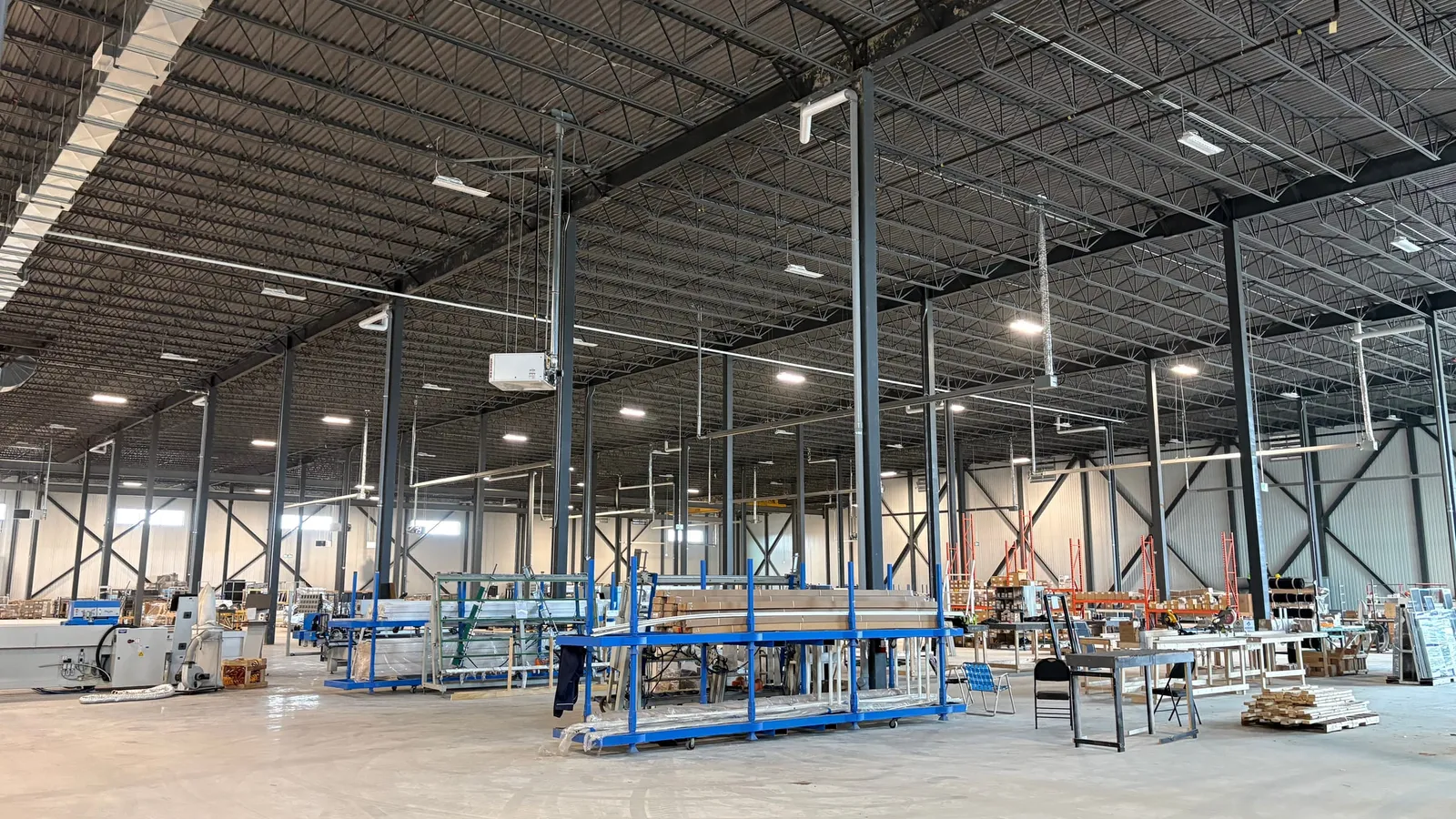 The finished interior of a large industrial building: a high open-web joist roof on steel columns, with a production line being set up on the floor.