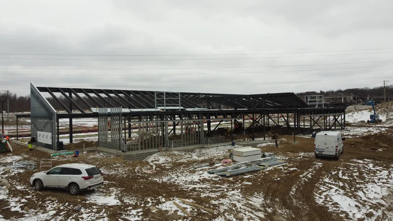 The front of the library's steel frame, with sloped roof members over steel-stud walls and a muddy, snowy site in front.