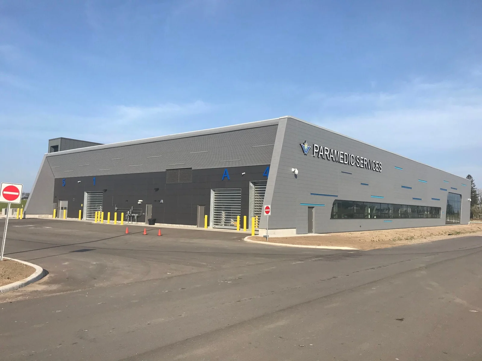 The finished paramedic services station: a long grey building with a sloped parapet, a row of overhead bay doors and a sign reading Paramedic Services.