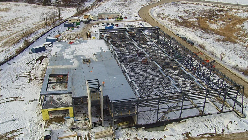 An aerial view of the station under construction in snow: the decked office block at the left and the open steel frame of the apparatus bays at the right.