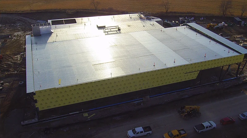 An aerial view of the building with its roof deck on and yellow sheathing on the walls, with pickups parked beside it.
